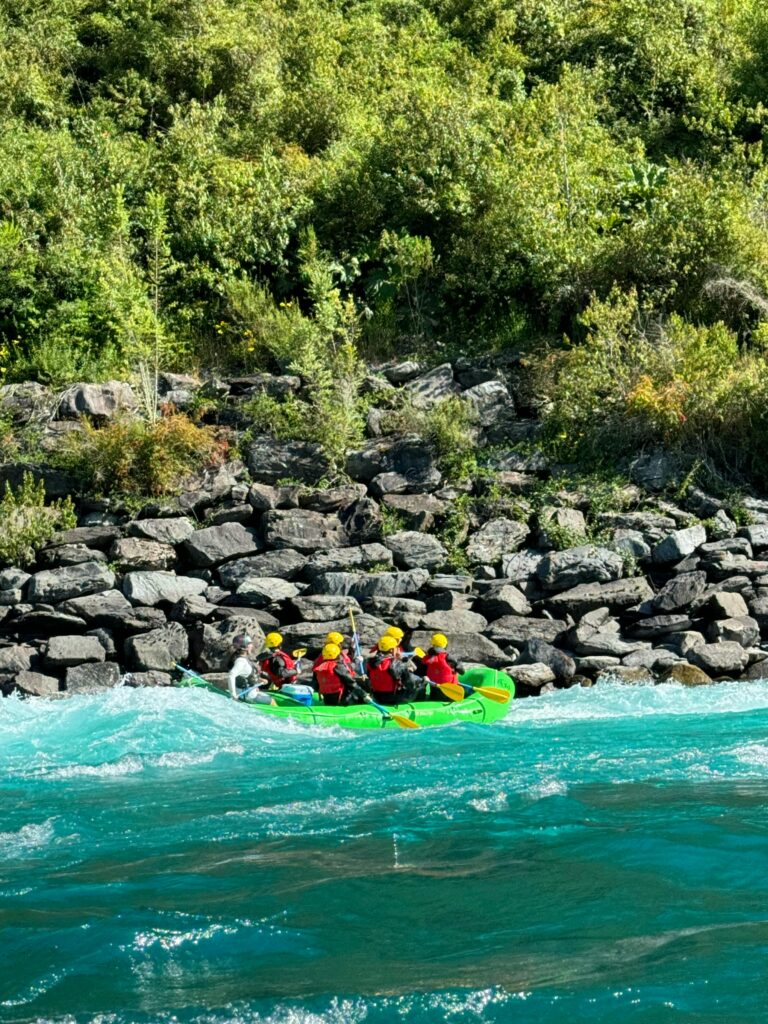 A group of people enjoying an exciting rafting adventure on a vibrant river surrounded by rocks and greenery.