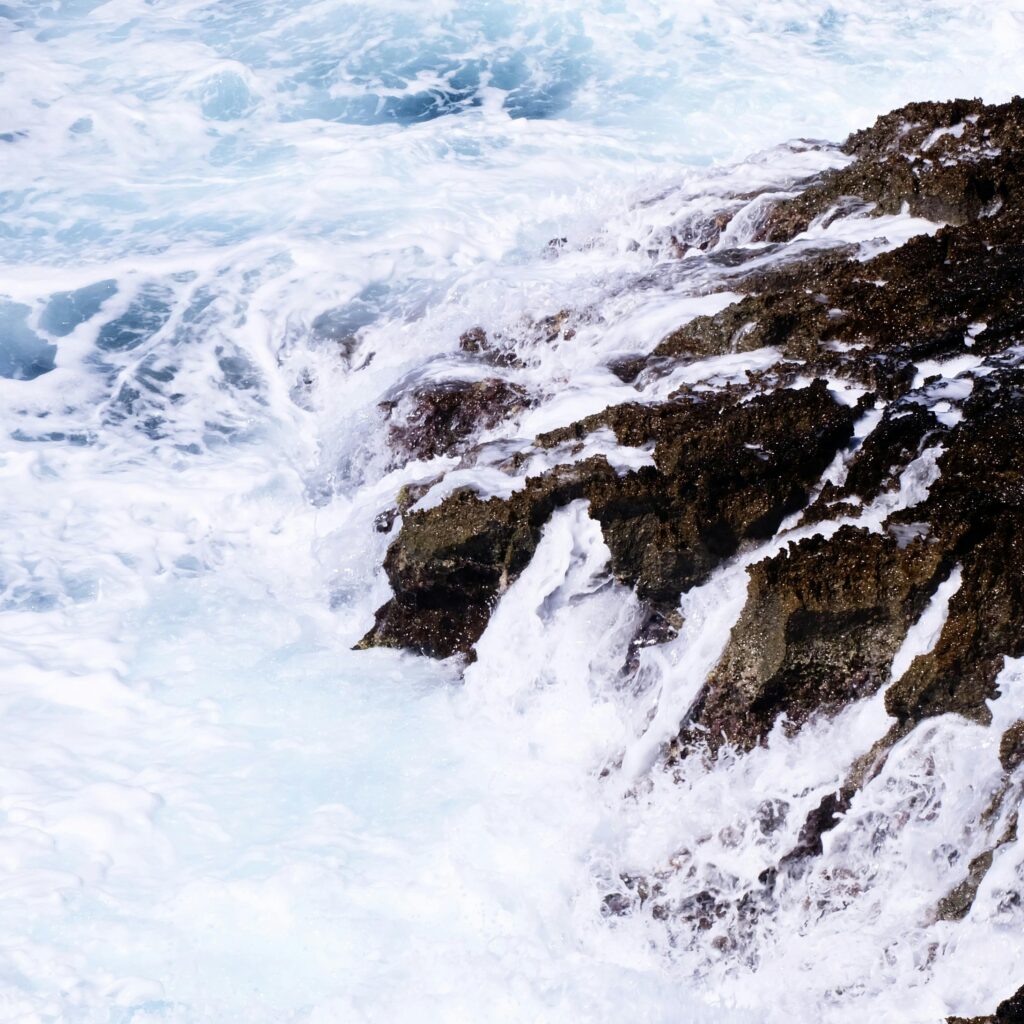 Vibrant ocean waves crash against rugged rocks, showcasing the raw power of nature.